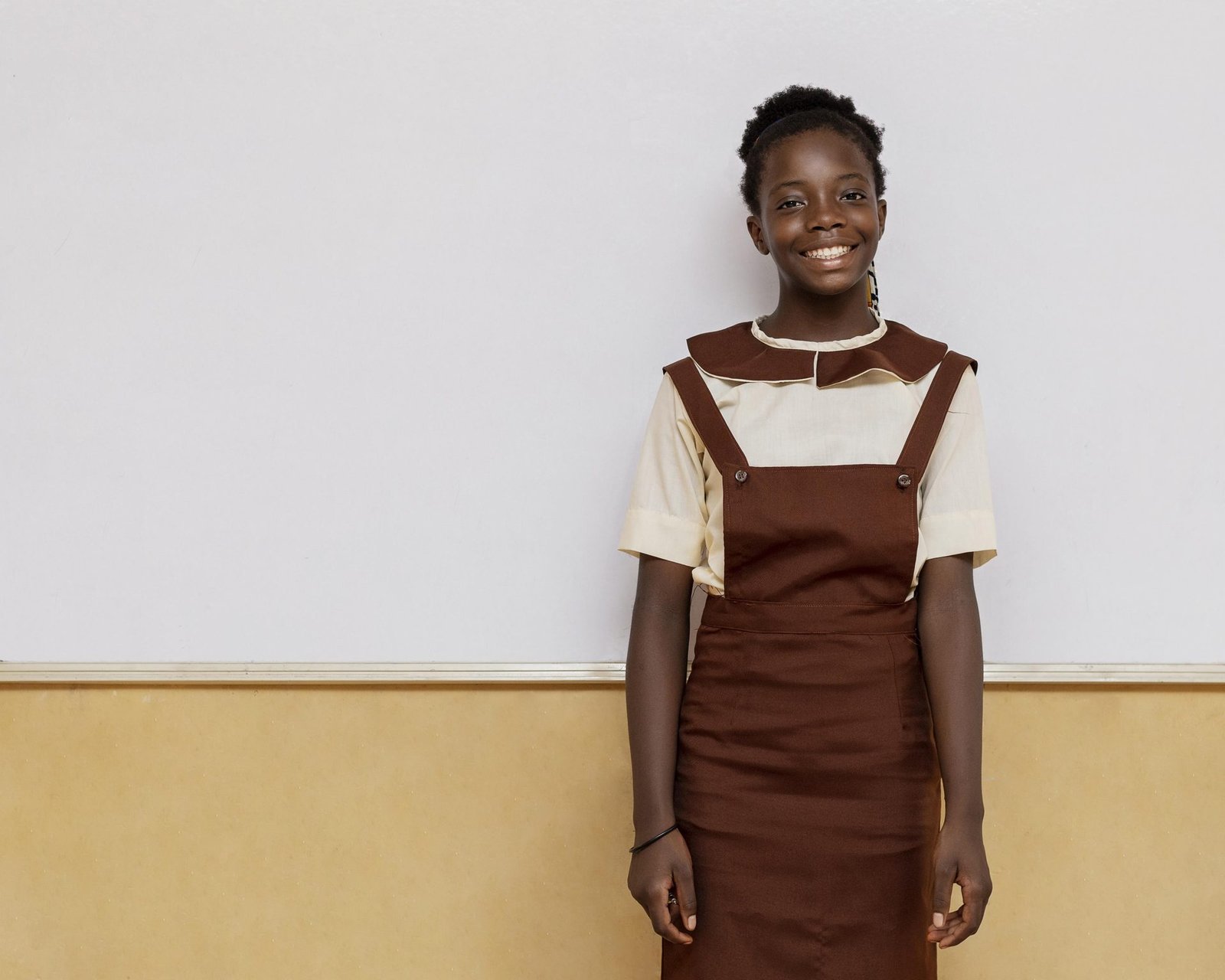 Portrait d'une écolière en uniforme devant le mur de sa classe