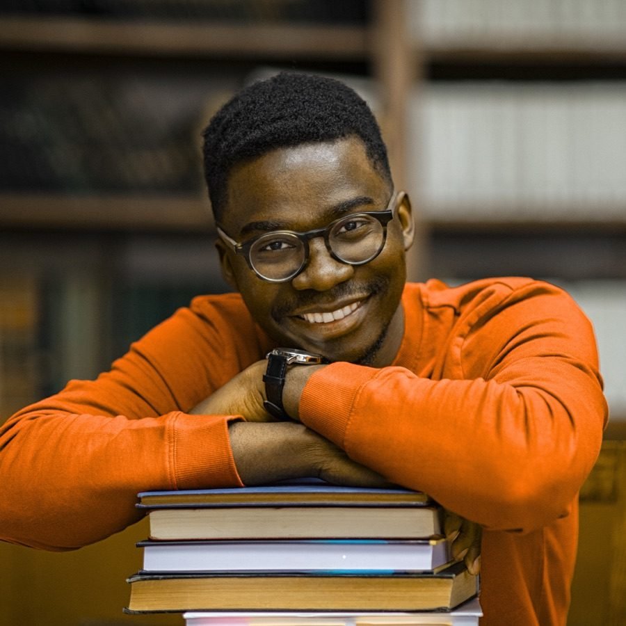Un étudiant souriant, accoudé à une pile de livres