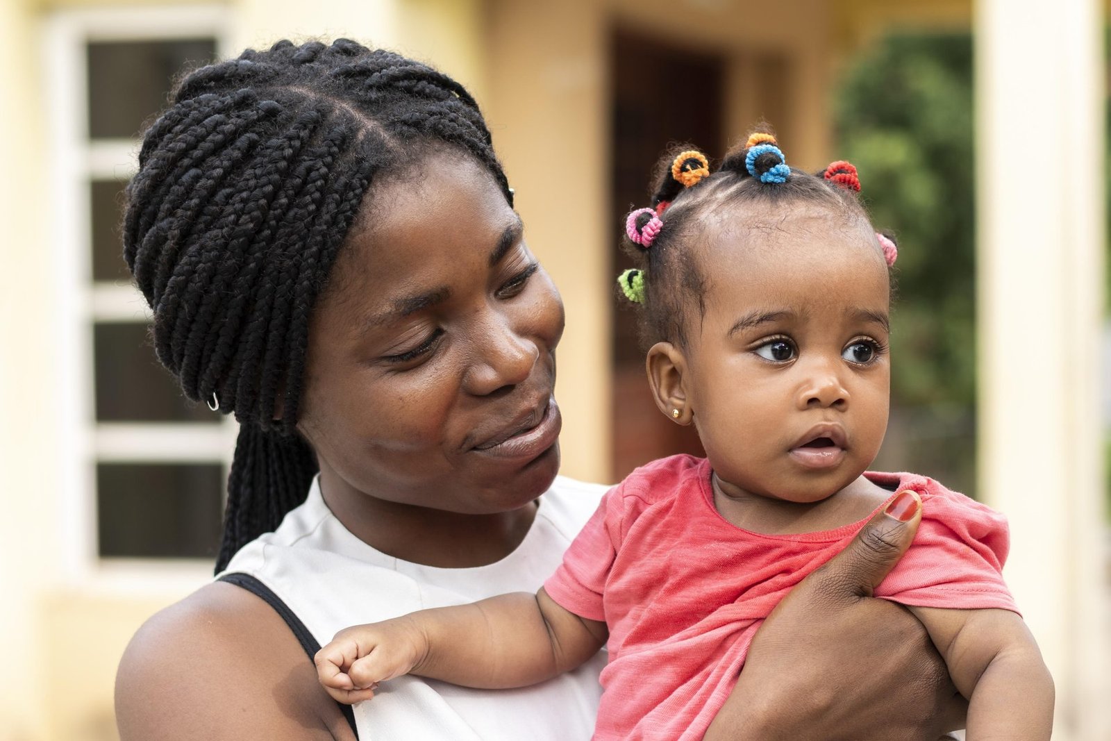 Une mère porte son jeune enfant dans ses bras devant leur maison