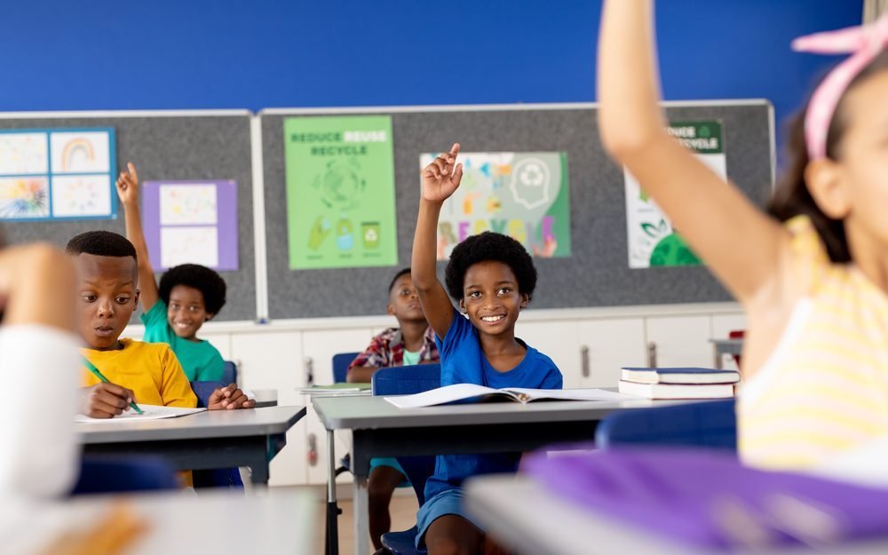 Des élèves d'école élémentaire lèvent la main dans leur classe