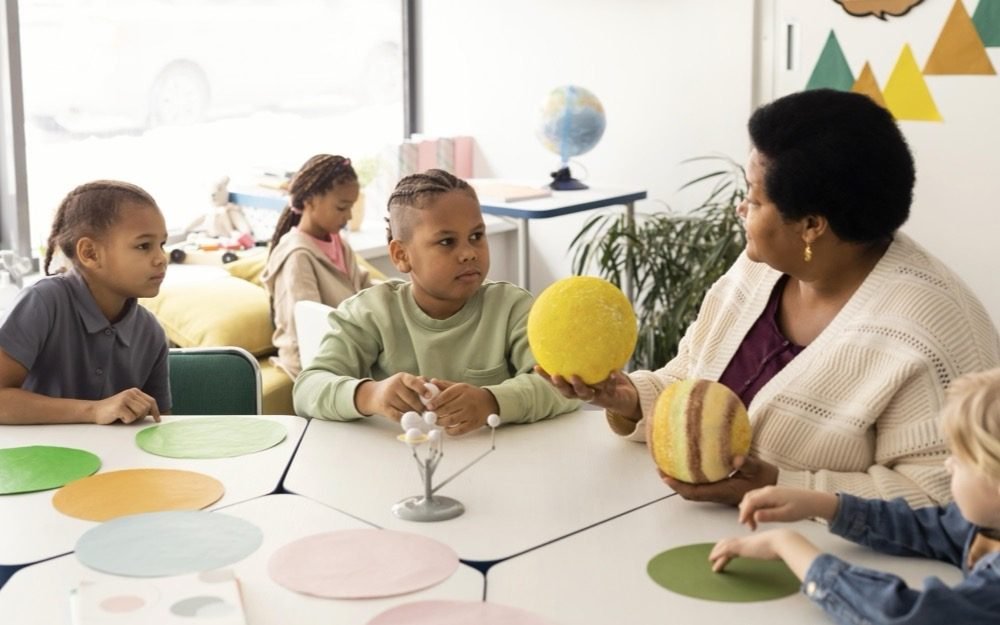 Une enseignante et de jeunes enfants autour d'une table d'activités en maternelle